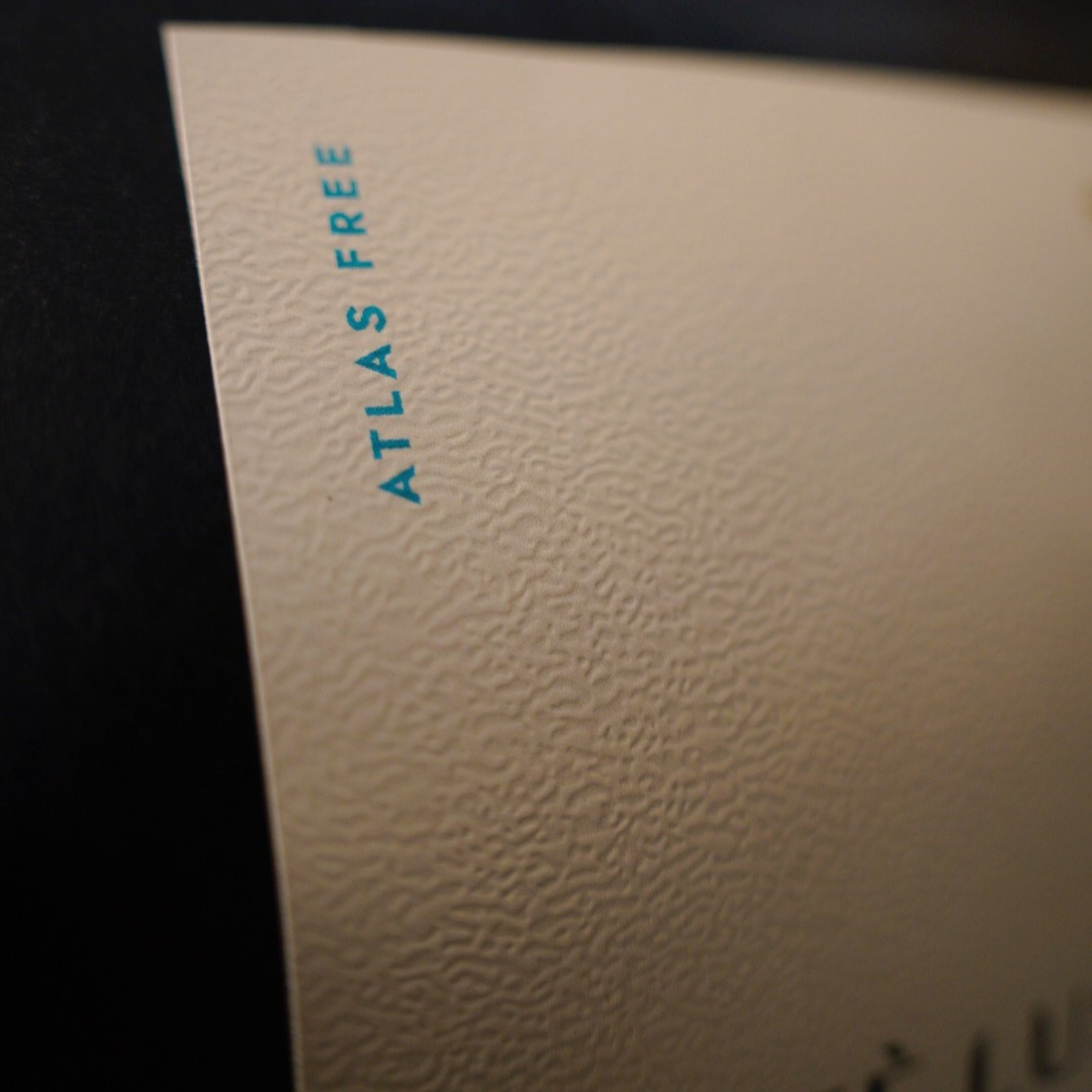 Close-up of a textured cream label with the words 'ATLAS FREE' printed vertically in blue near the upper left, against a dark background.