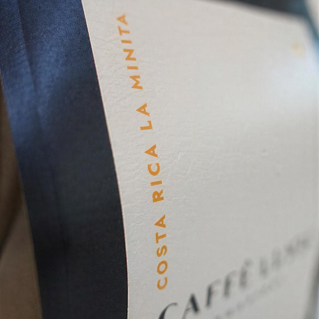 Close-up of a coffee package label with the text 'COSTA RICA LA MINITA' printed vertically in orange on an off-white background