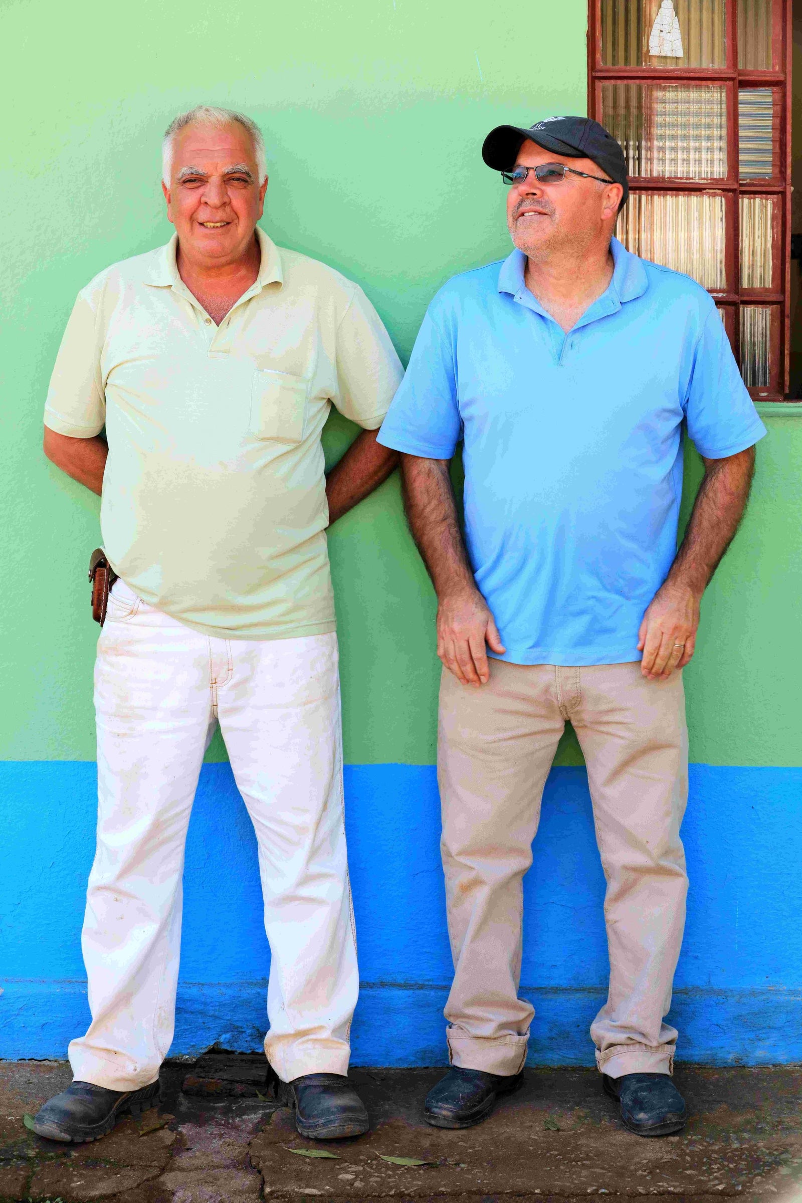 Two Brazilian farmers smile for a picture in front of a colorful wall.