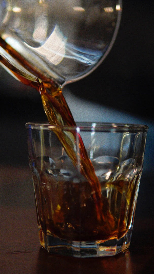 a glass of coffee being poured from a chemex coffee maker