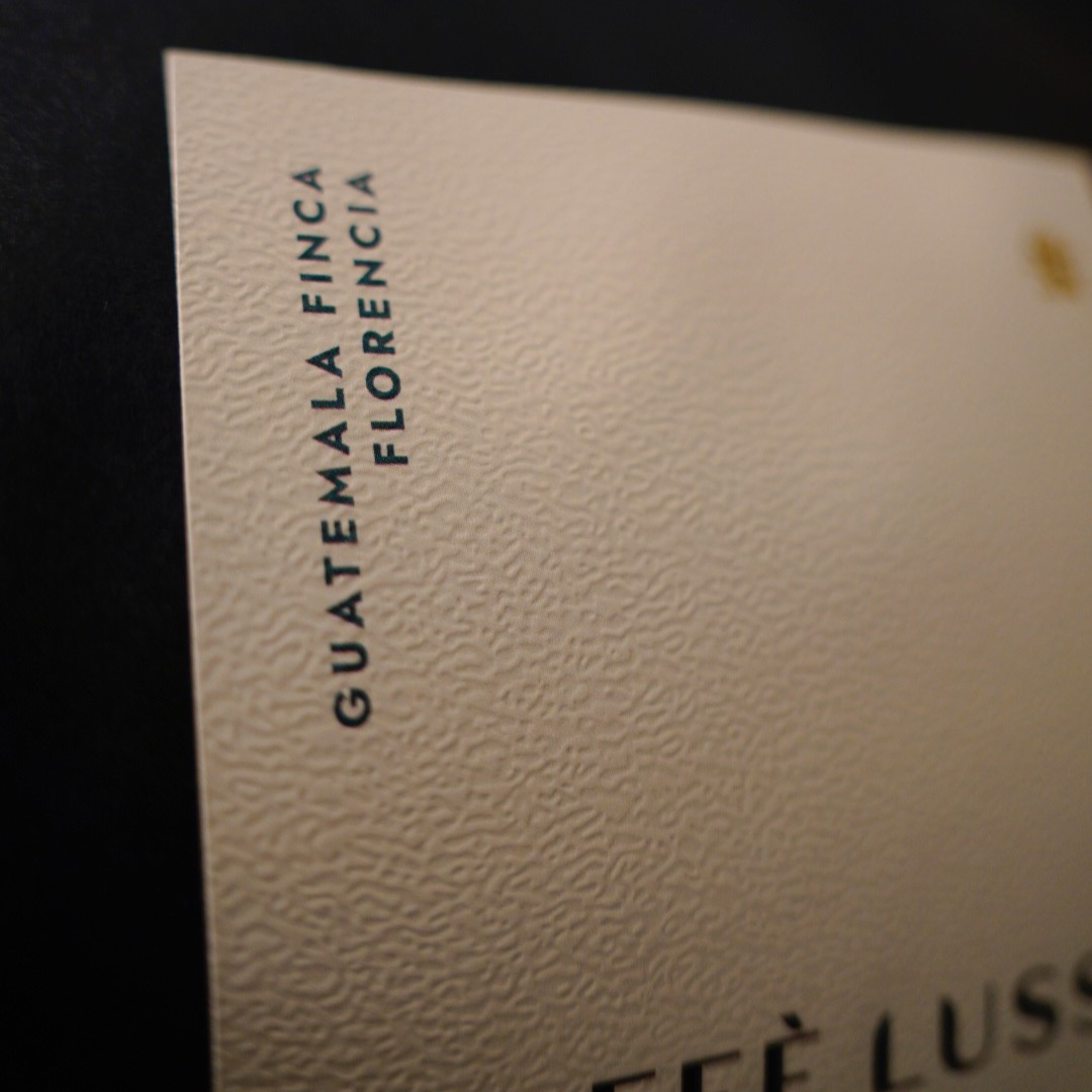 Close-up of a textured cream-colored label with vertical black text reading 'GUATEMALA FINCA FLORENCIA' against a dark background.