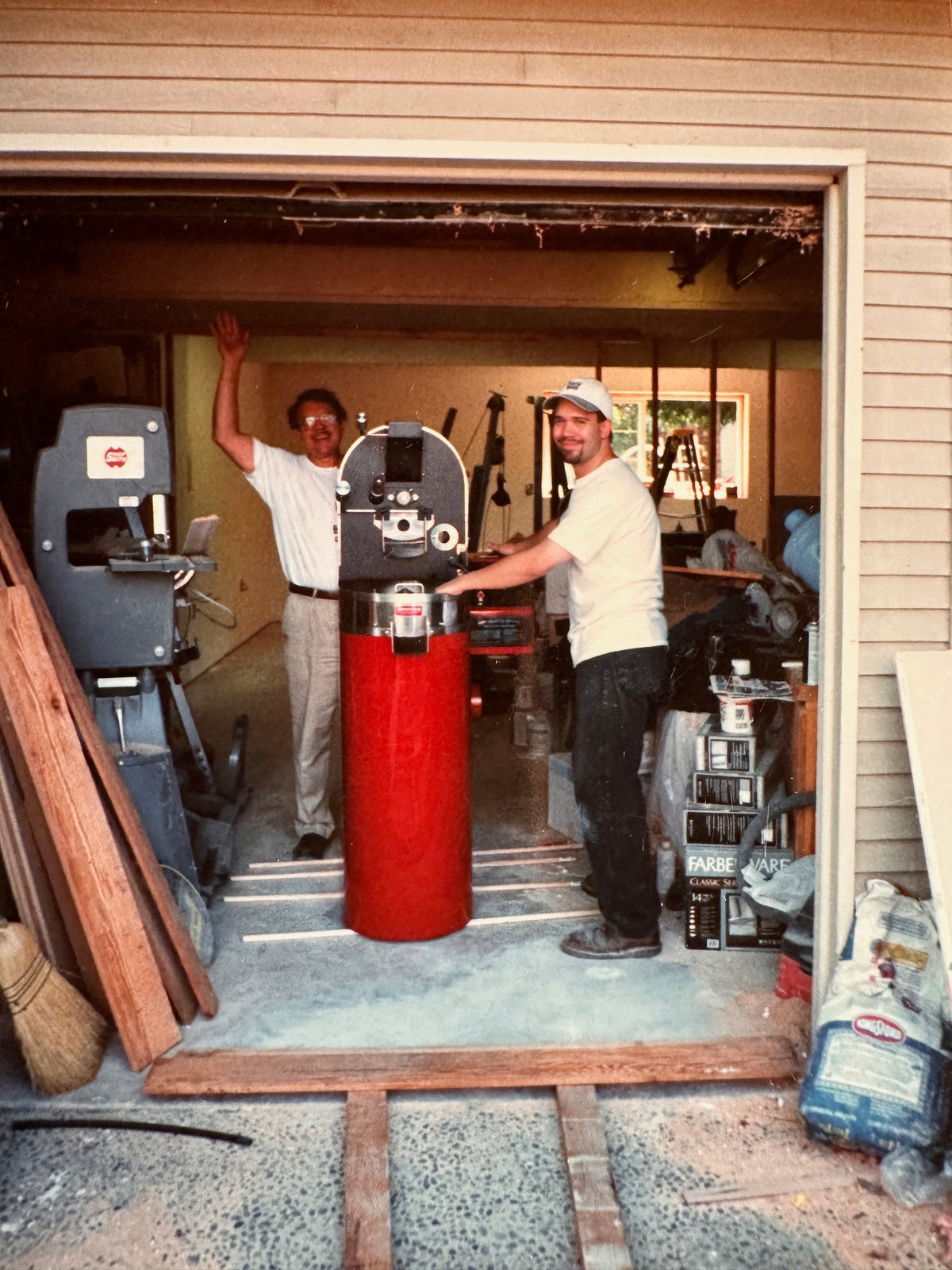 Philip and his Father Wayne standing in the first edition of Caffe Lusso Roastery, their home garage. They are standing with a small red roasting machine.
