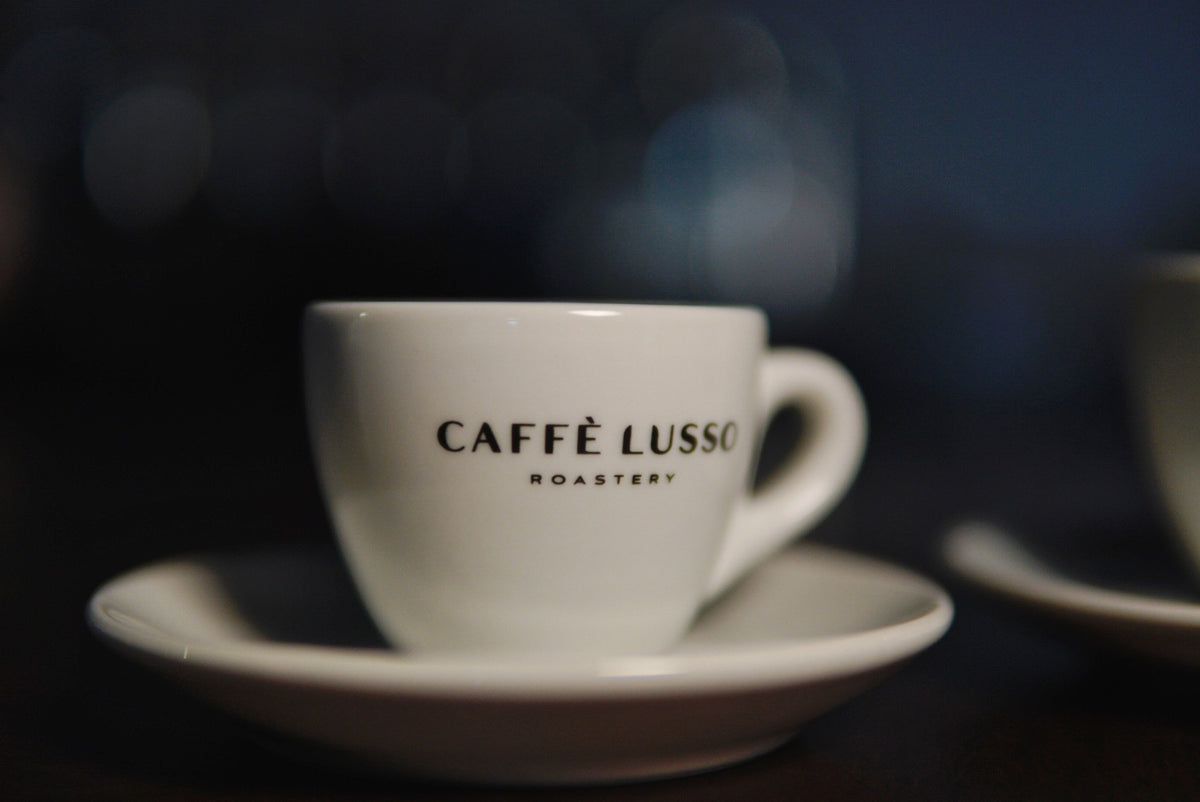 White porceline demitasse cup with hite saucer, Caffe Lusso Logo on front