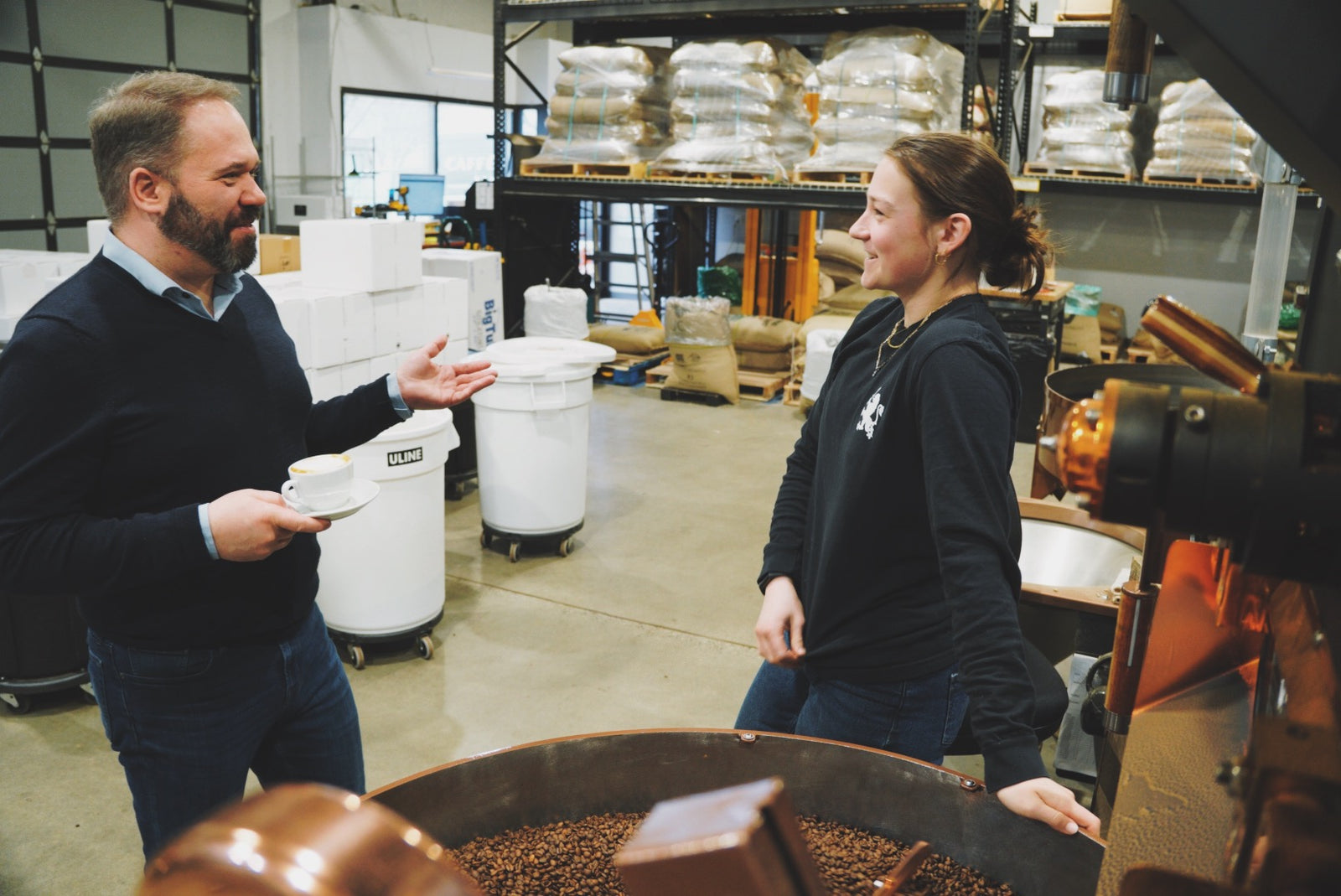 Philip and Emma discussing coffee roasting over the coffee roaster cooling tray in the roastery