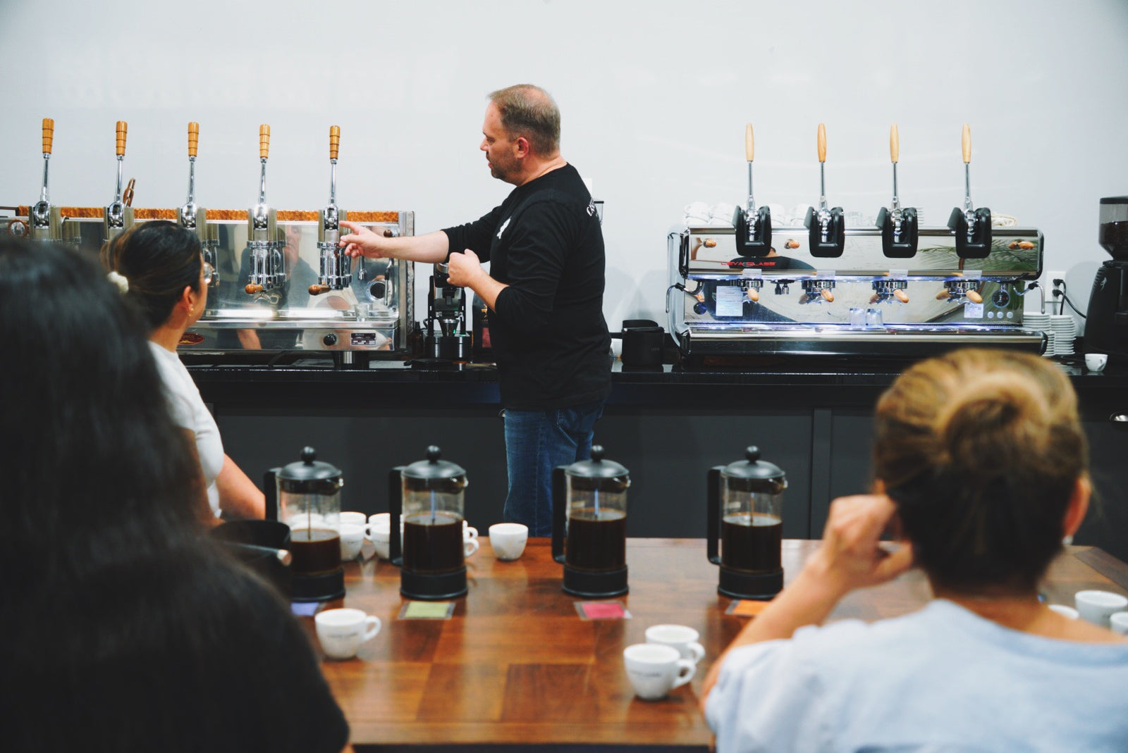 a man instrucs people on  lever espresso machine while they drink coffee