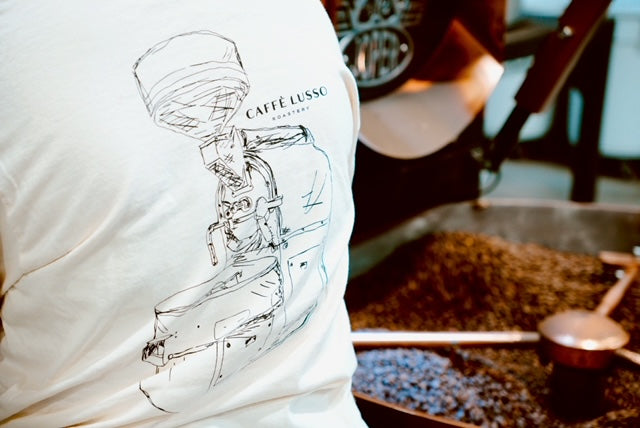 A person wearing a white, heavy weight ring spun cotton tee with a hand sketched drawing of a coffee roasting machine on the back.