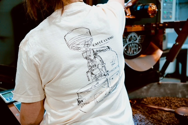 A person wearing a white, heavy weight ring spun cotton tee with a hand sketched drawing of a coffee roasting machine on the back.