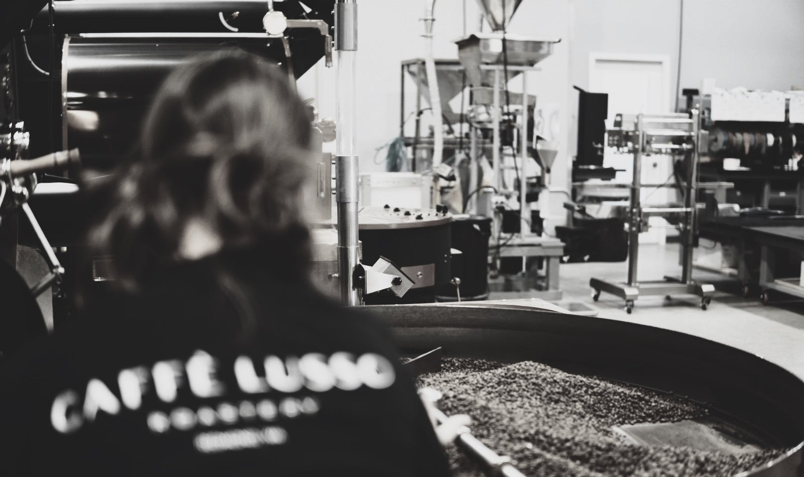 A woman roasting coffee while looking at the cooling tray.