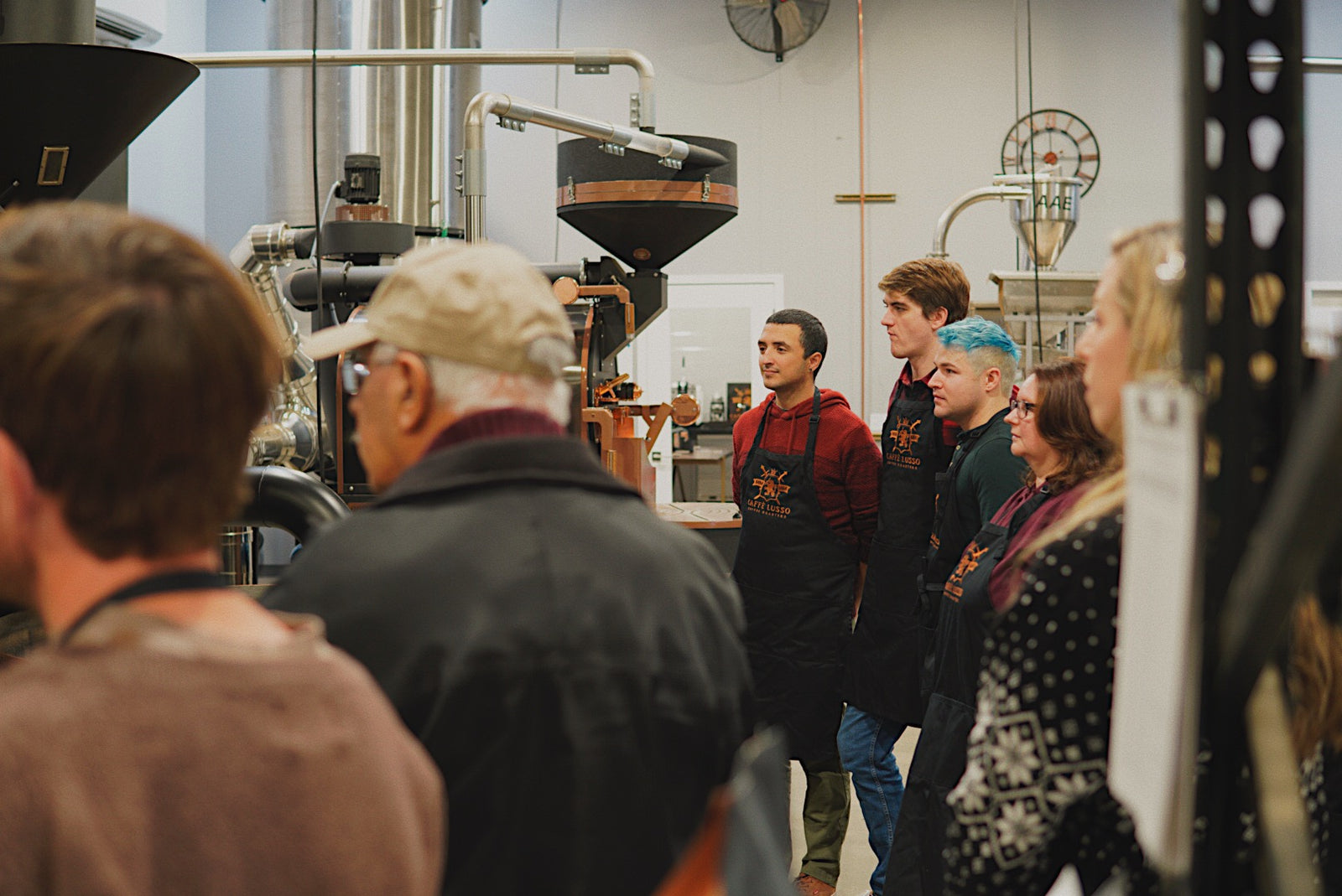 A group of people in a roastery listening to a demonstration of coffee roasting