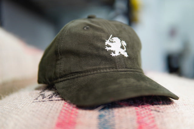 Olive Green Hat with an Embroidered Lion. Sitting on a coffee bag