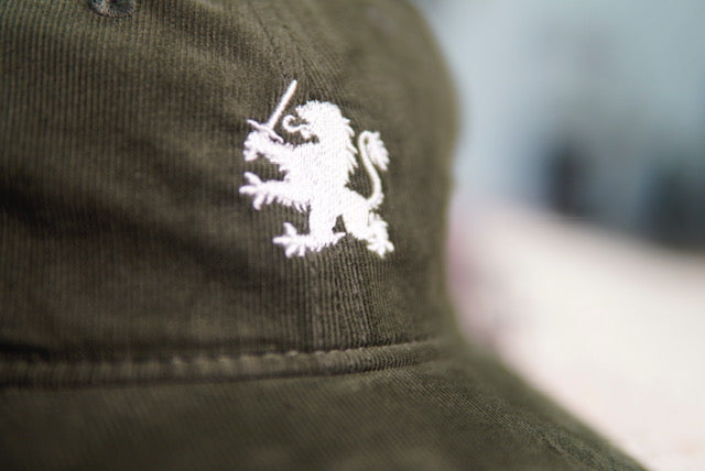 Olive Green Hat with an Embroidered Lion. Sitting on a coffee bag